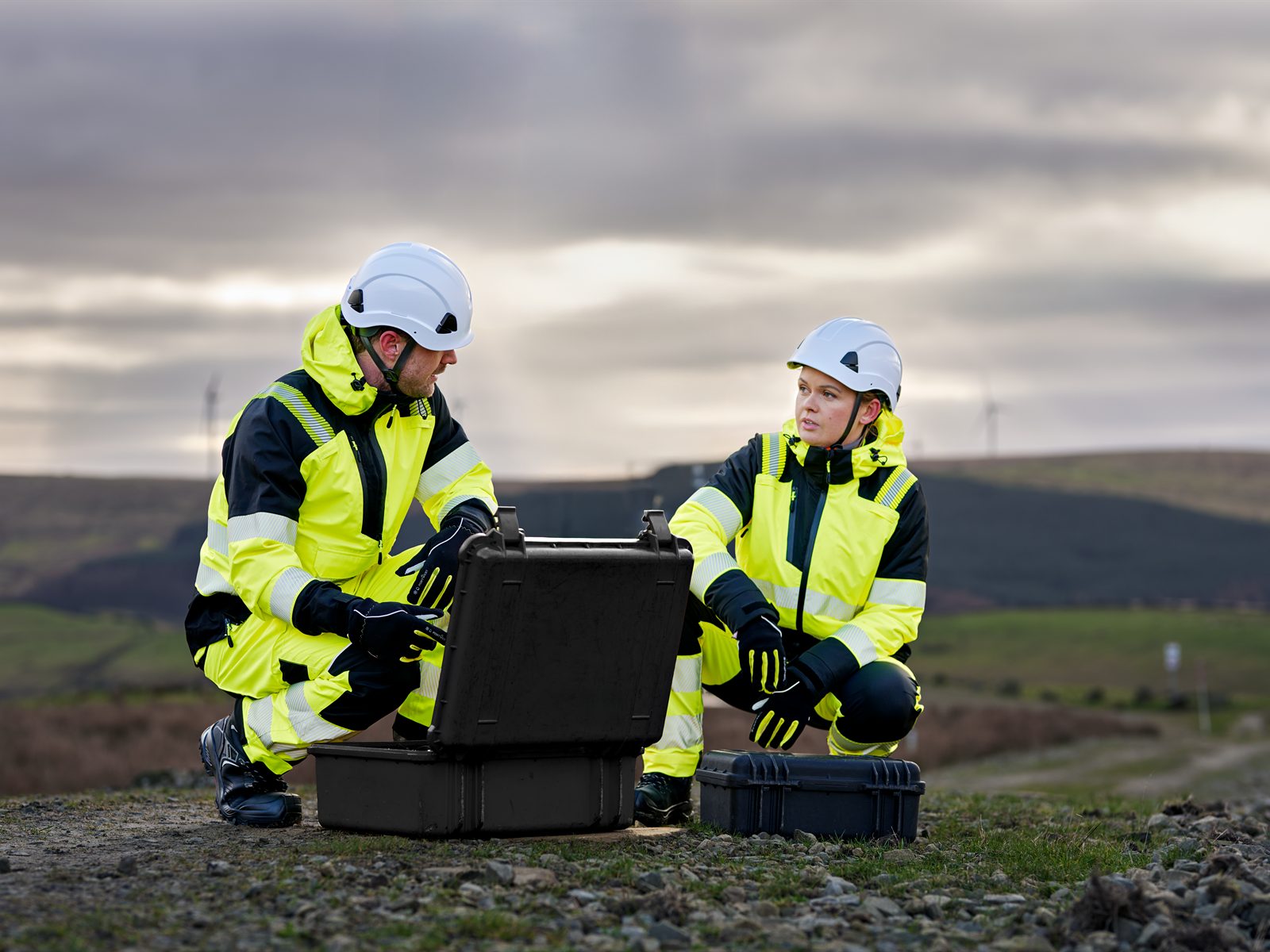 Two PPE-equipped workers preparing equipment at an outdoor worksite