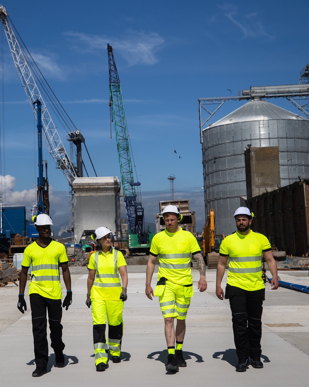 Four PPE-equipped workers walking through an industrial construction site
